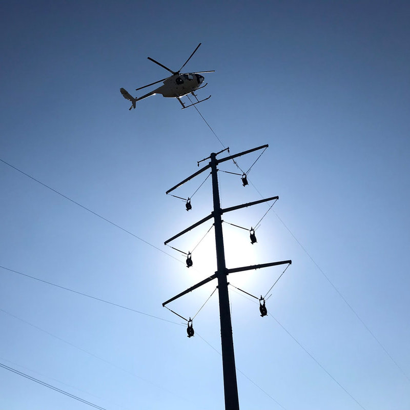 Utility helicopter supporting a wire pull operation above a steel pole transmission structure.